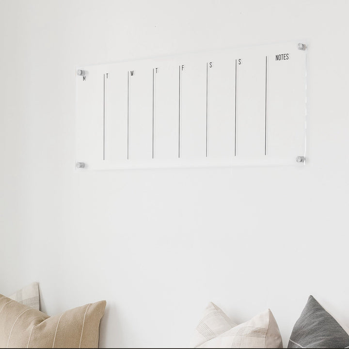 A skinny dry-erase weekly calender made of acrylic hanging on the wall