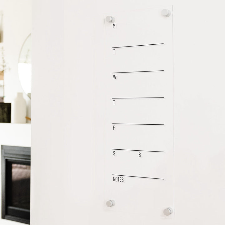 A skinny dry-erase weekly calender made of acrylic hanging on the wall