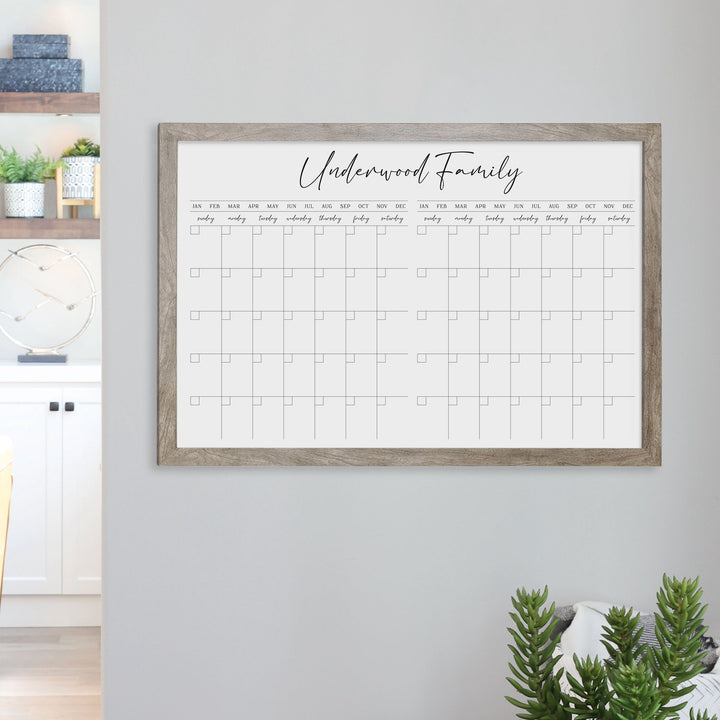 A framed whiteboard calendar with a two month design format hanging on the wall
