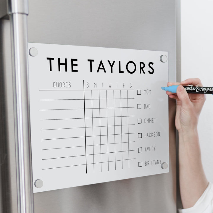 A Dry-erase magnetic acrylic chore chart hanging on the fridge