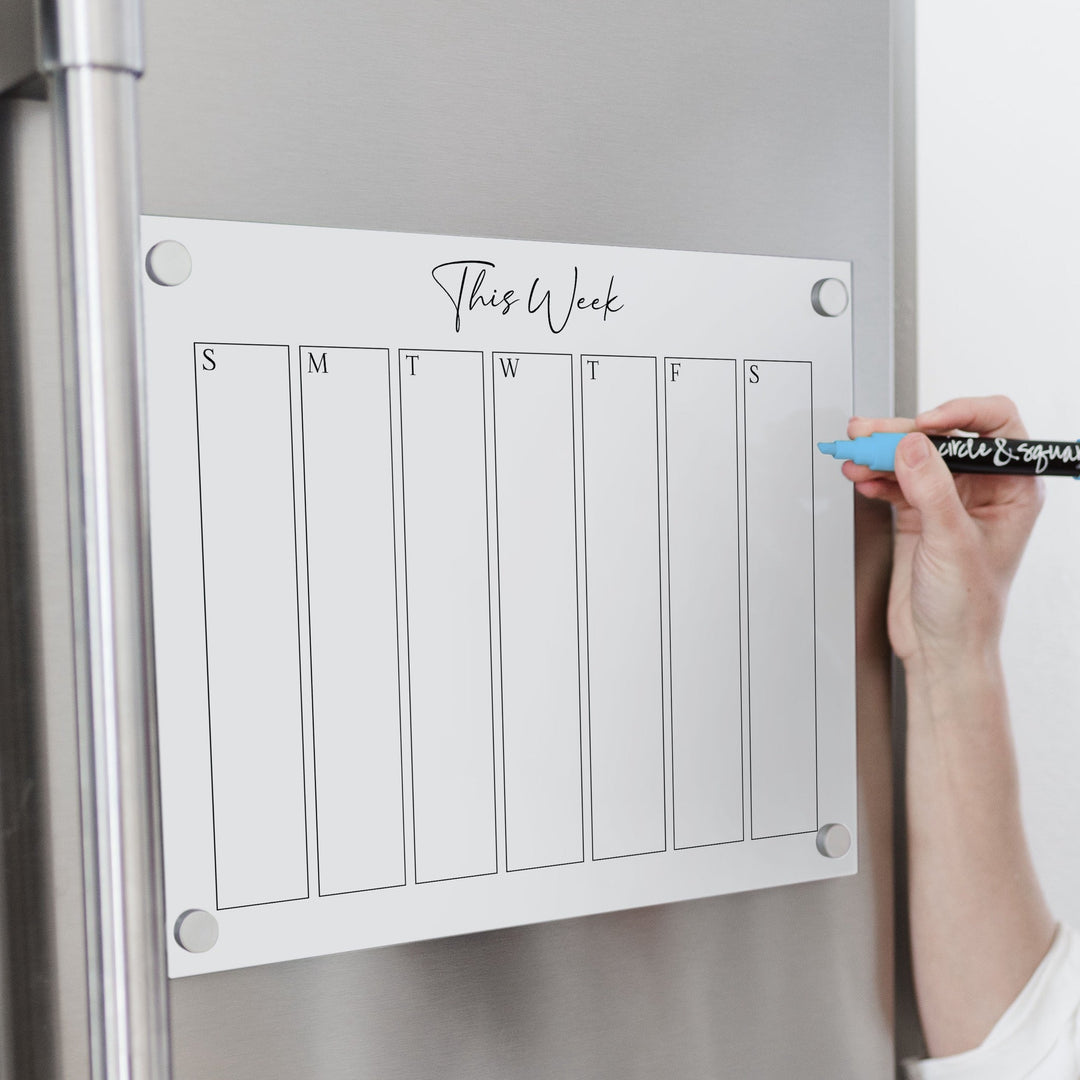 A skinny dry-erase weekly calender made of magnetic acrylic hanging on the fridge
