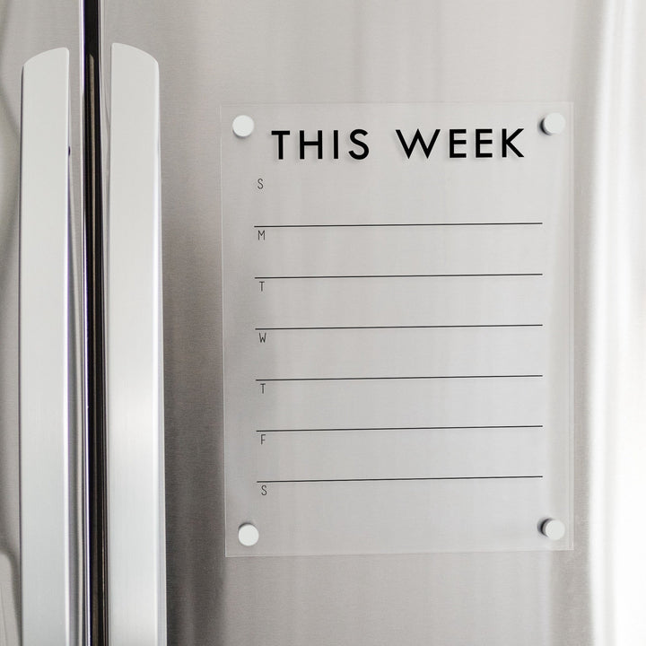 A skinny dry-erase weekly calender made of magnetic acrylic hanging on the fridge