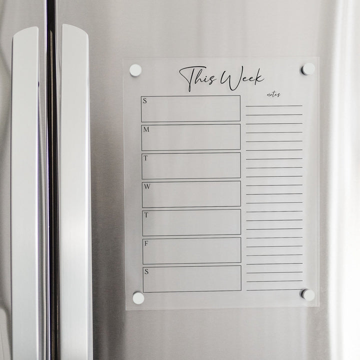 A skinny dry-erase weekly calender made of magnetic acrylic hanging on the fridge