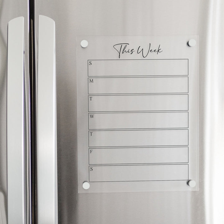 A skinny dry-erase weekly calender made of magnetic acrylic hanging on the fridge