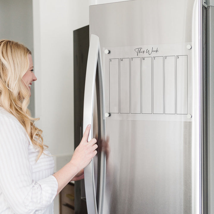 A skinny dry-erase weekly calender made of magnetic acrylic hanging on the fridge