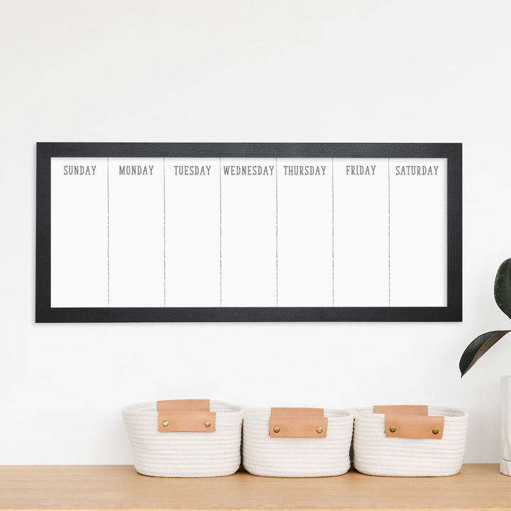 A framed slim whiteboard weekly calender hanging on the wall