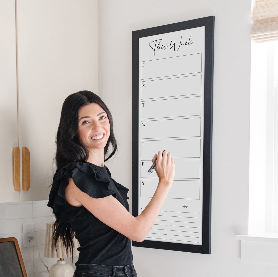 A framed slim whiteboard weekly calender hanging on the wall