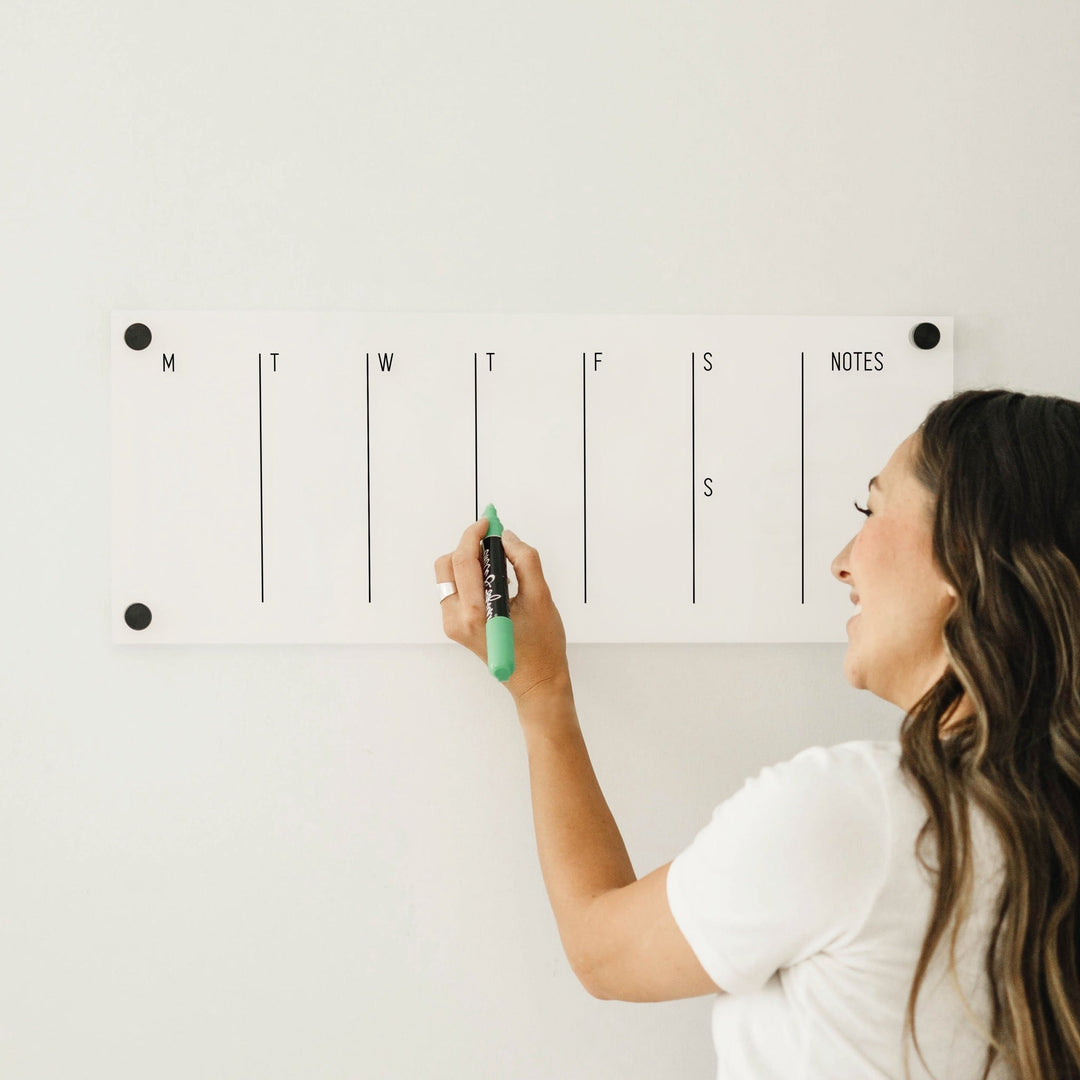 A skinny dry-erase weekly calender made of acrylic hanging on the wall