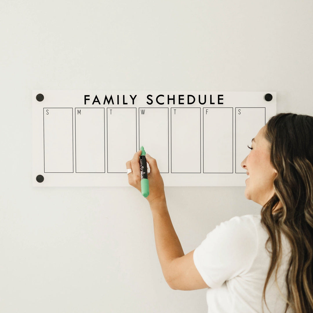 A skinny dry-erase weekly calender made of acrylic hanging on the wall