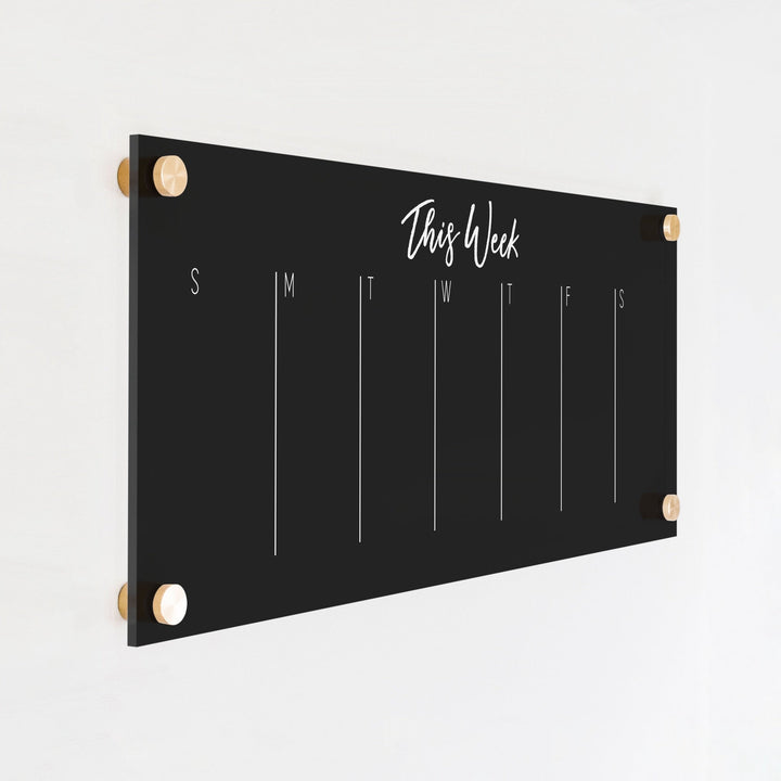 A skinny dry-erase weekly calender made of acrylic hanging on the wall