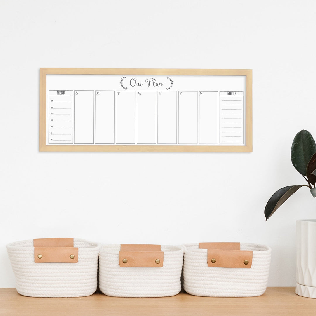 A framed slim dry-erase weekly calender with a faux chalkboard look hanging on the wall