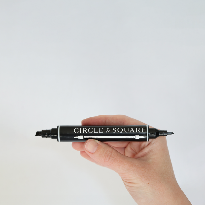 a hand holds the multi tip chalk marker to show the chisel tip and the fine tip