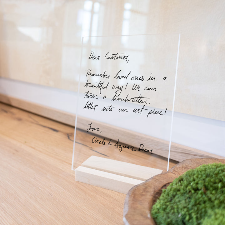 A handwriting memorial keepsake on clear acrylic with a blonde wooden stand.