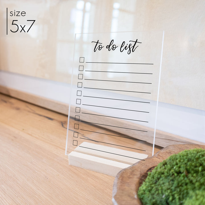 A 5x7 simple to do list with a blonde wooden stand on an entryway table.