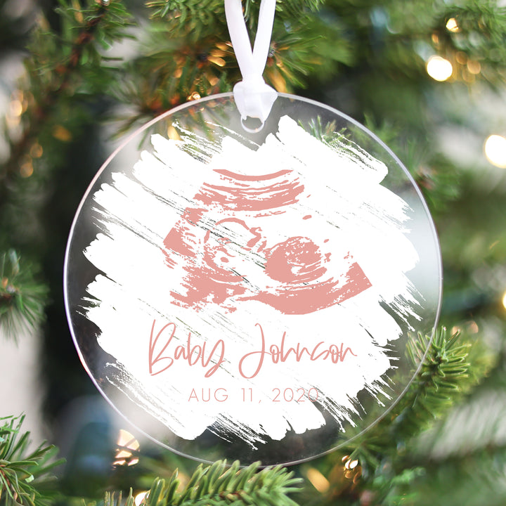 A Christmas ornament featuring a pink ultrasound on a white brushed background.