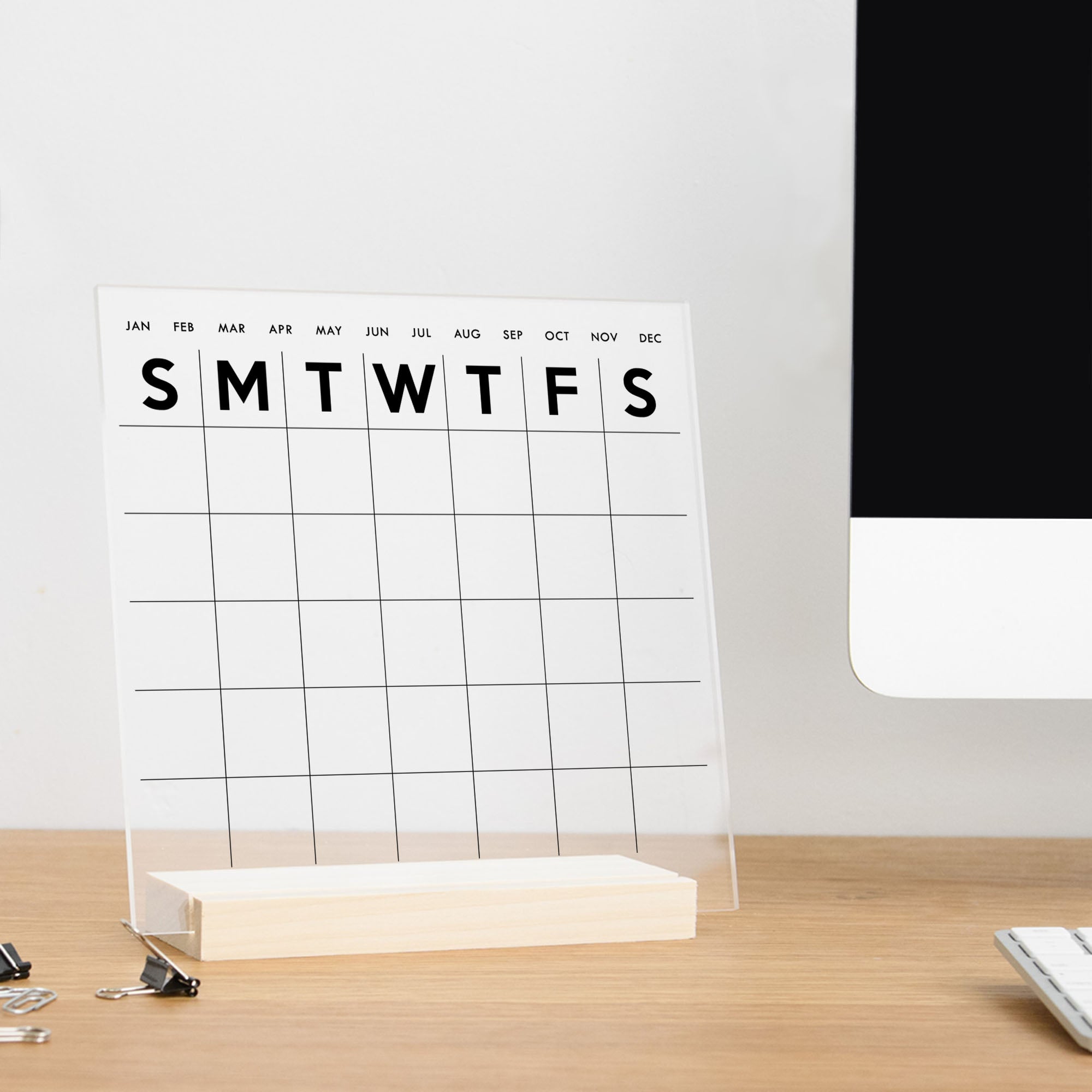 A simple acrylic calendar with a wooden stand on an office desk.