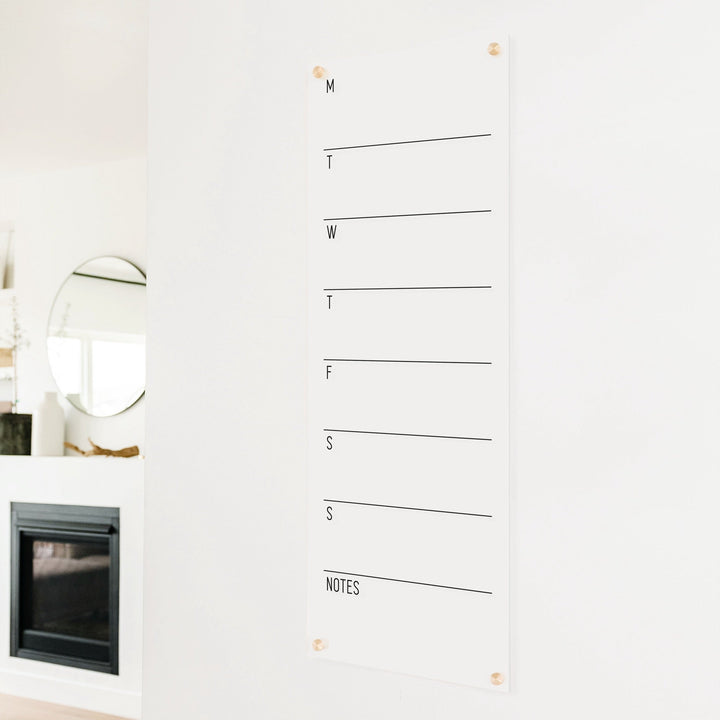 A skinny dry-erase weekly calender made of acrylic hanging on the wall