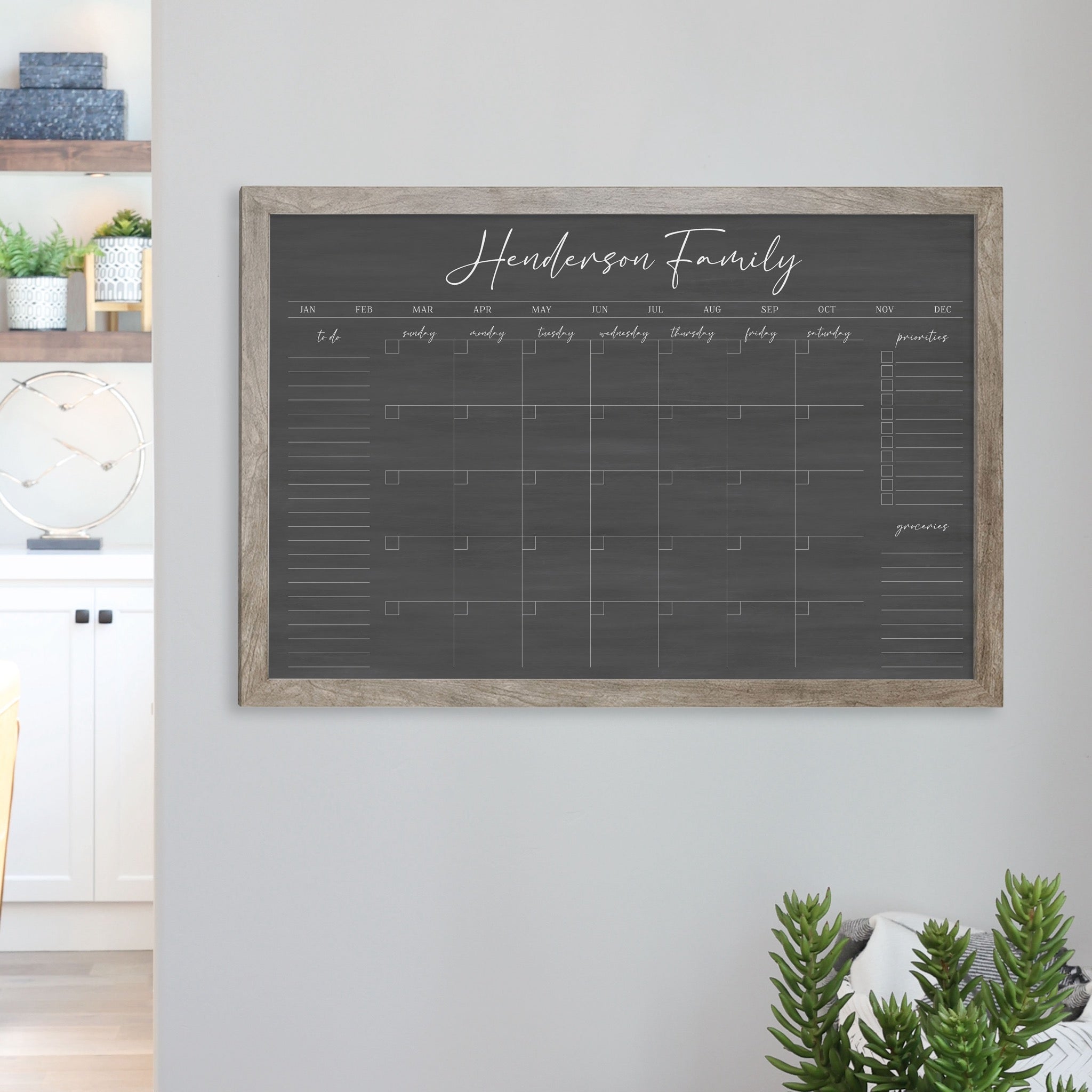 A framed dry-erase monthly calender with a chalkboard look hanging on the wall