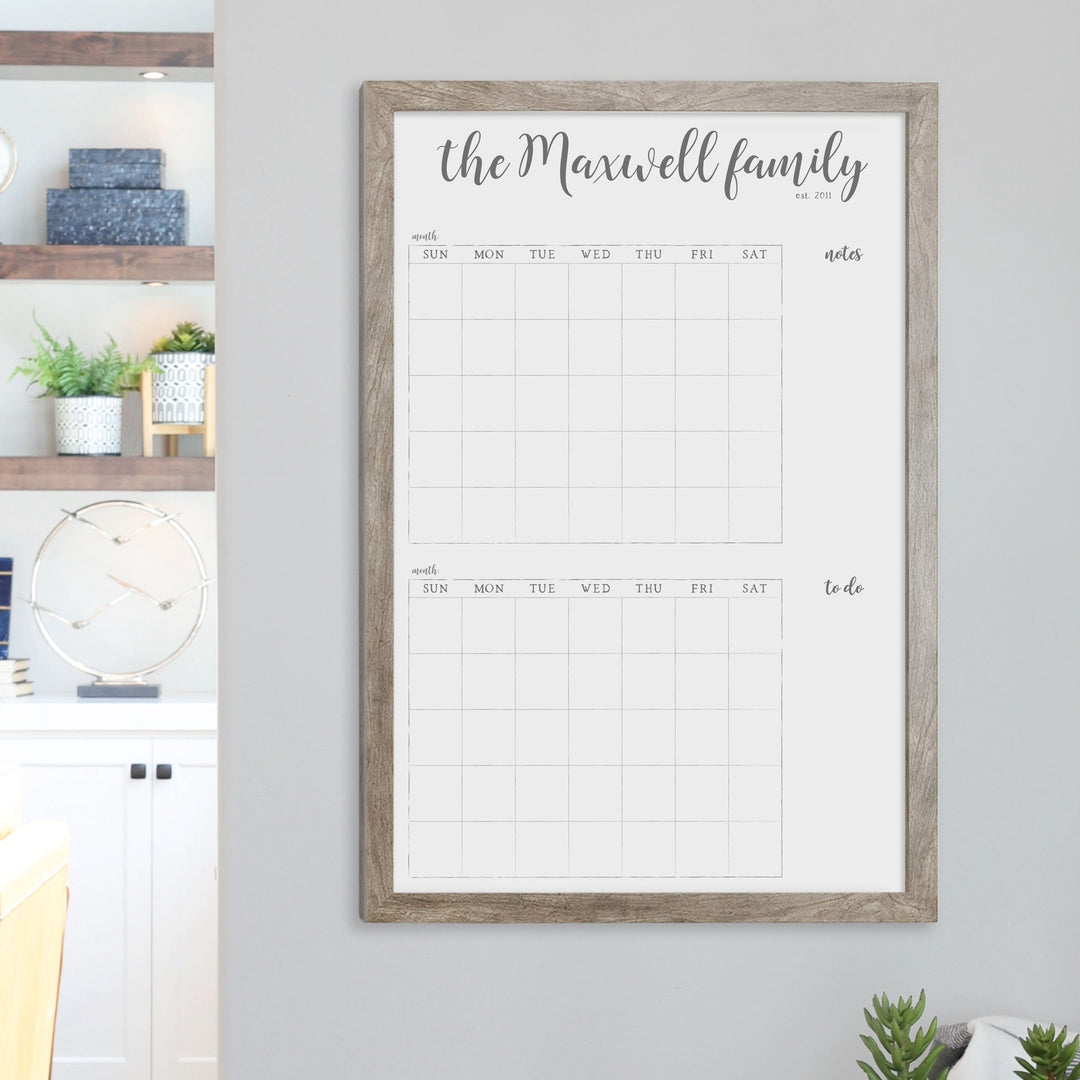 A framed whiteboard calendar with a two month design format hanging on the wall