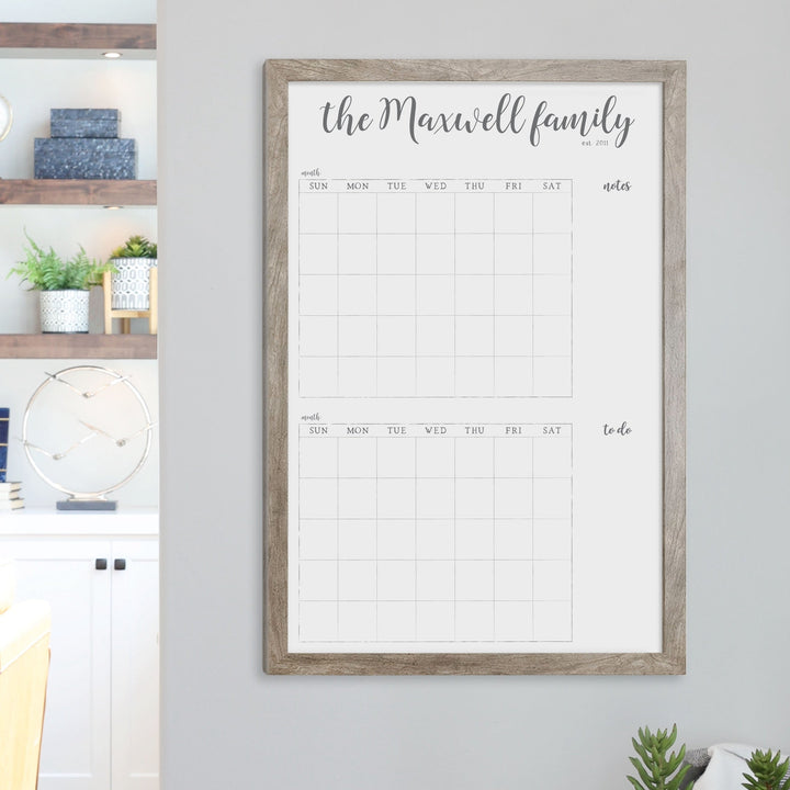 A framed whiteboard calendar with a two month design format hanging on the wall