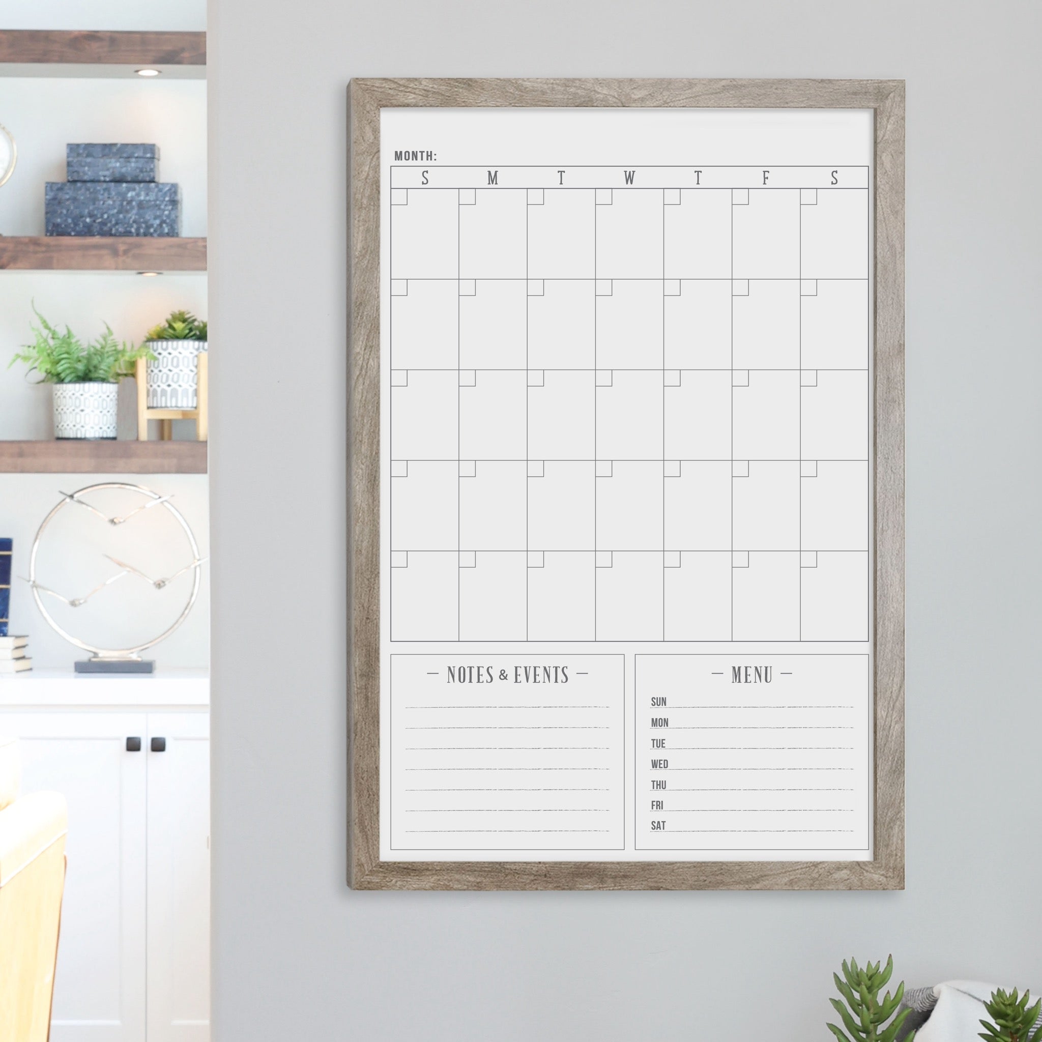 A framed dry-erase monthly calender with a chalkboard look hanging on the wall