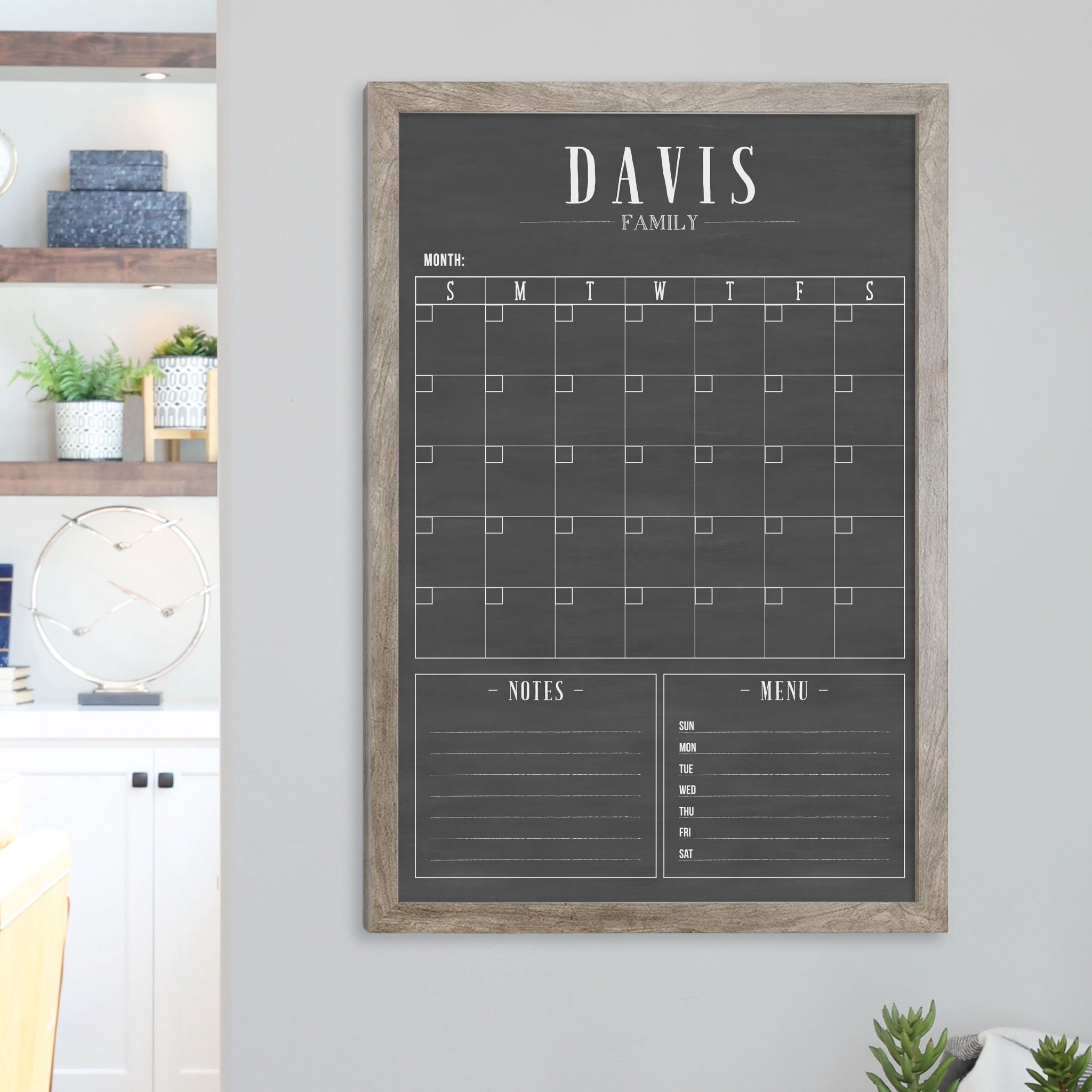 A framed dry-erase monthly calender with a chalkboard look hanging on the wall