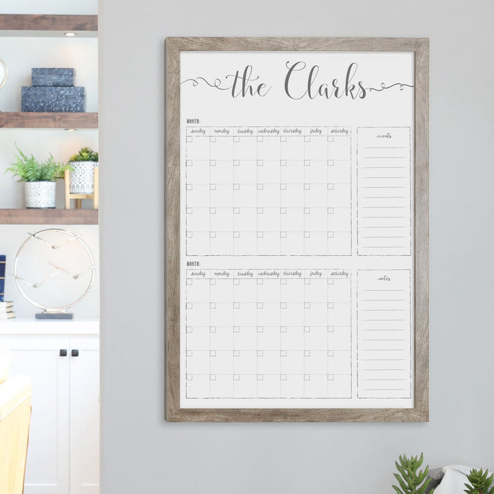 A framed whiteboard calendar with a two month design format hanging on the wall