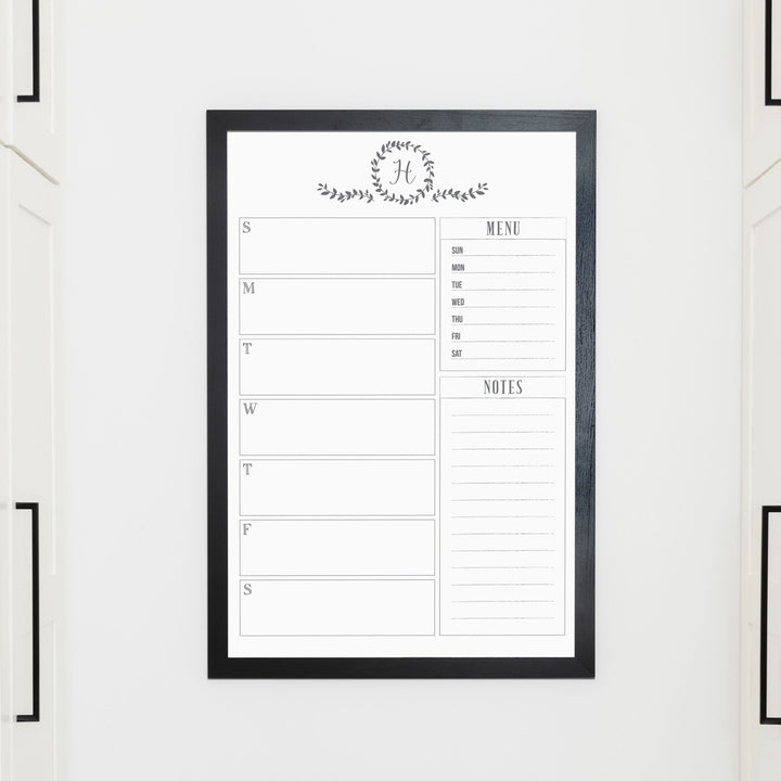 A framed whiteboard weekly calender hanging on the wall