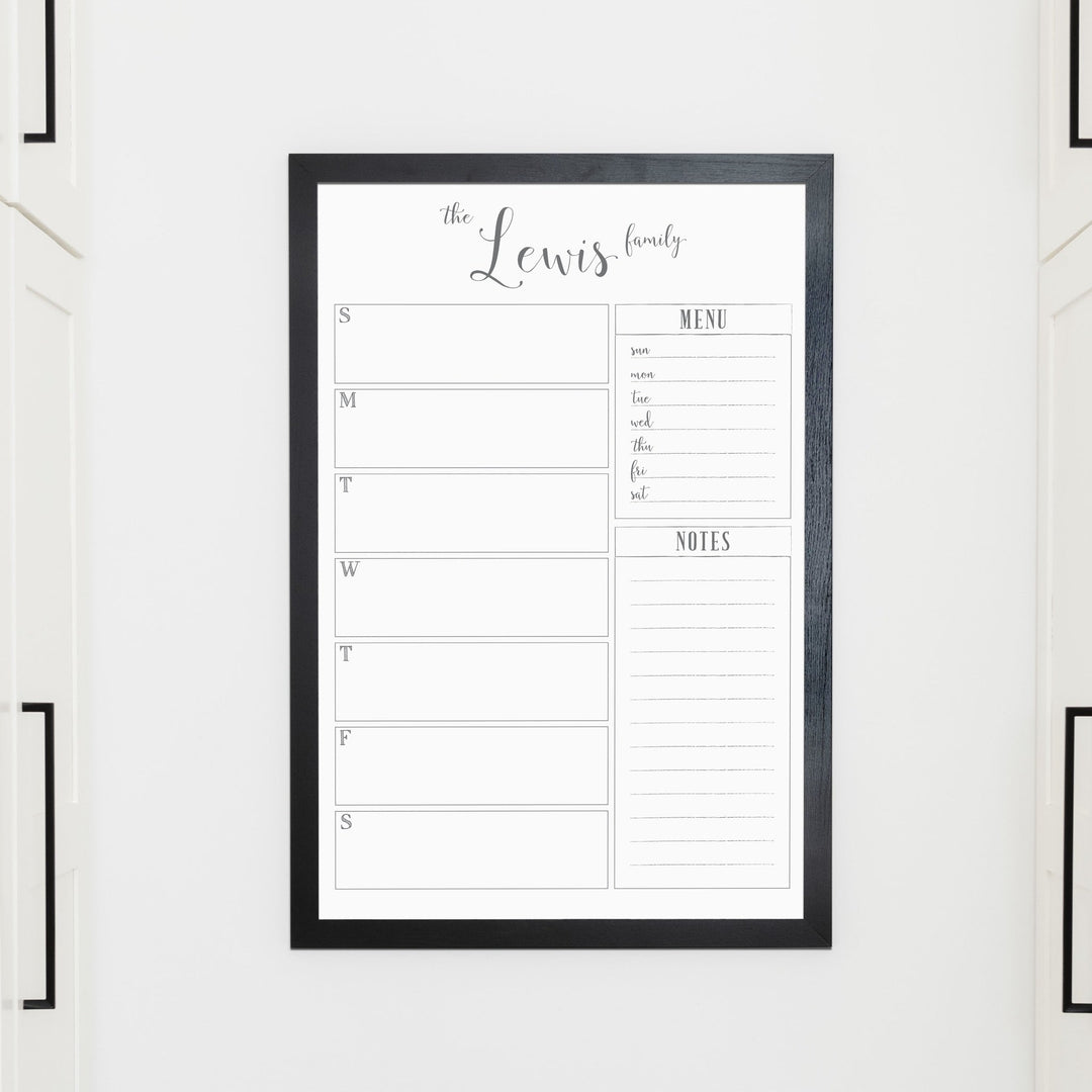 A framed whiteboard weekly calender hanging on the wall