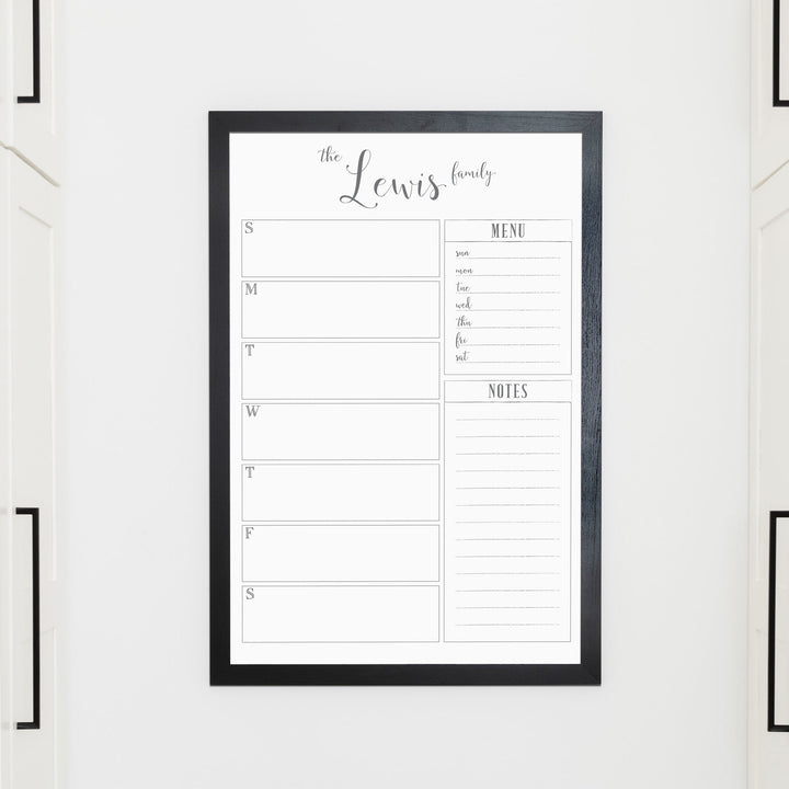 A framed whiteboard weekly calender hanging on the wall