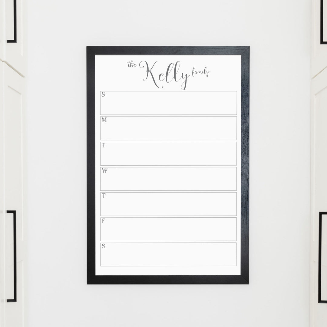 A framed whiteboard weekly calender hanging on the wall