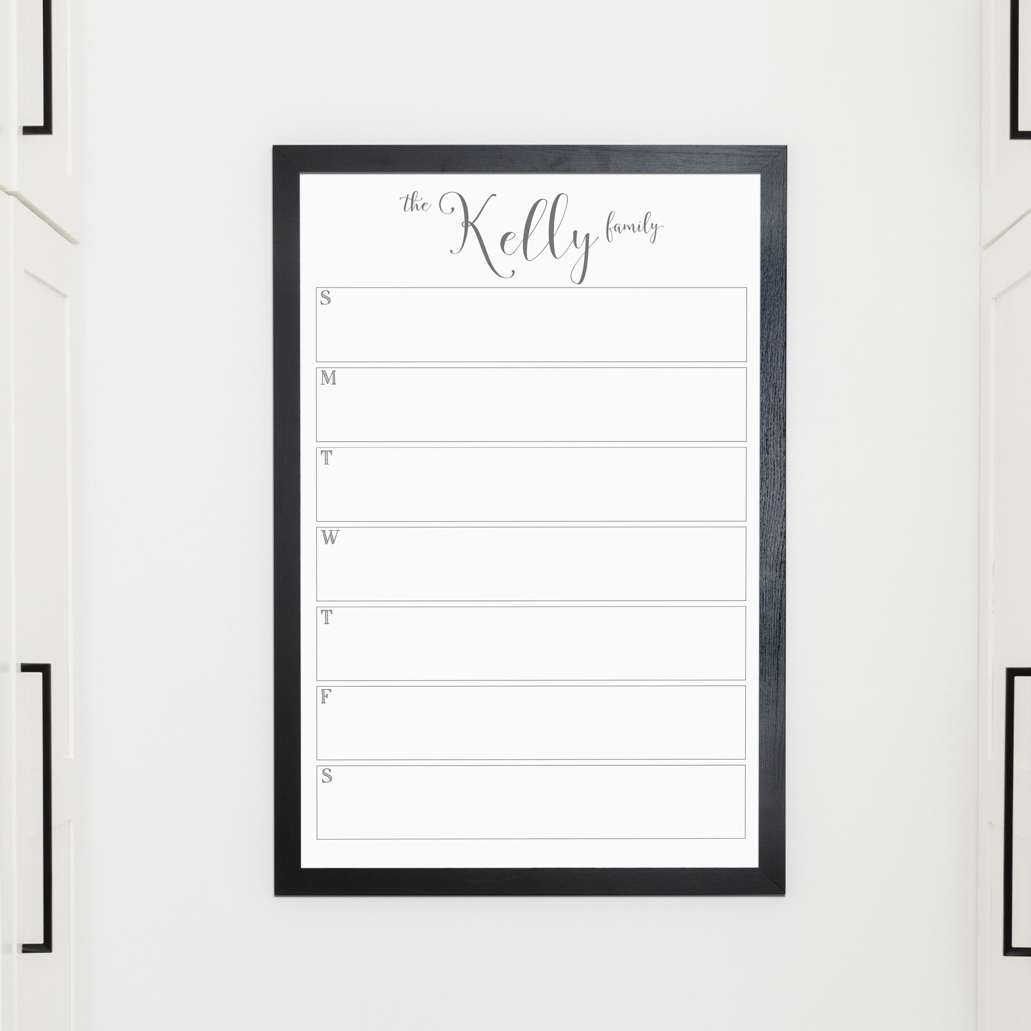 A framed whiteboard weekly calender hanging on the wall
