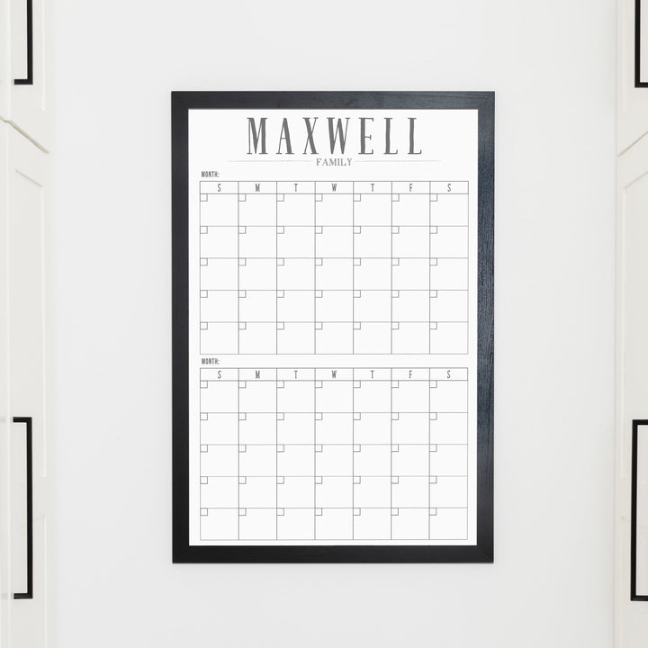 A framed whiteboard calendar with a two month design format hanging on the wall