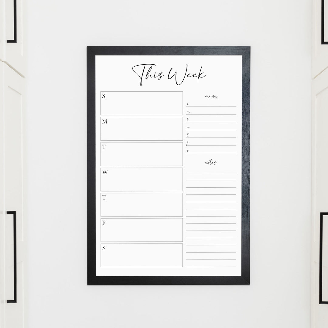 A framed whiteboard weekly calender hanging on the wall