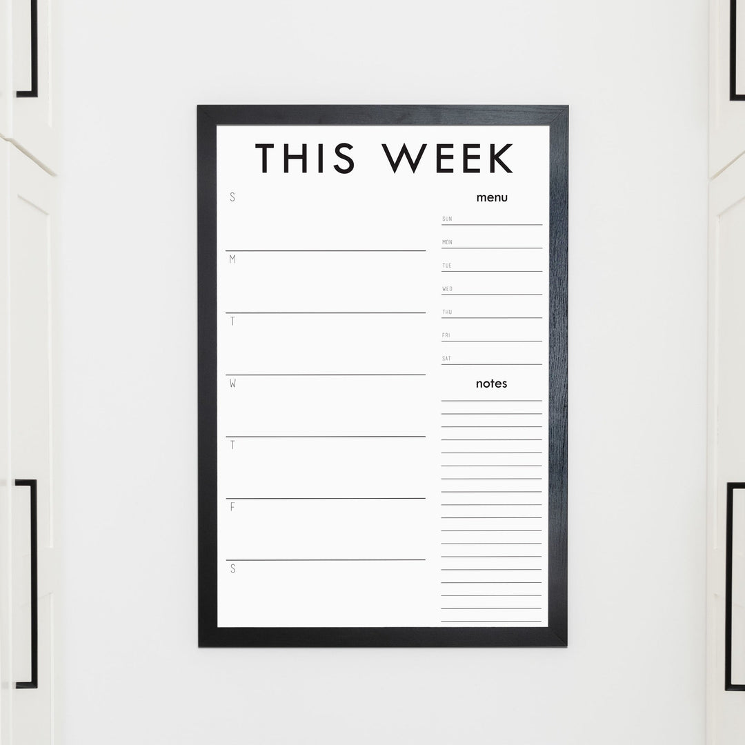 A framed whiteboard weekly calender hanging on the wall