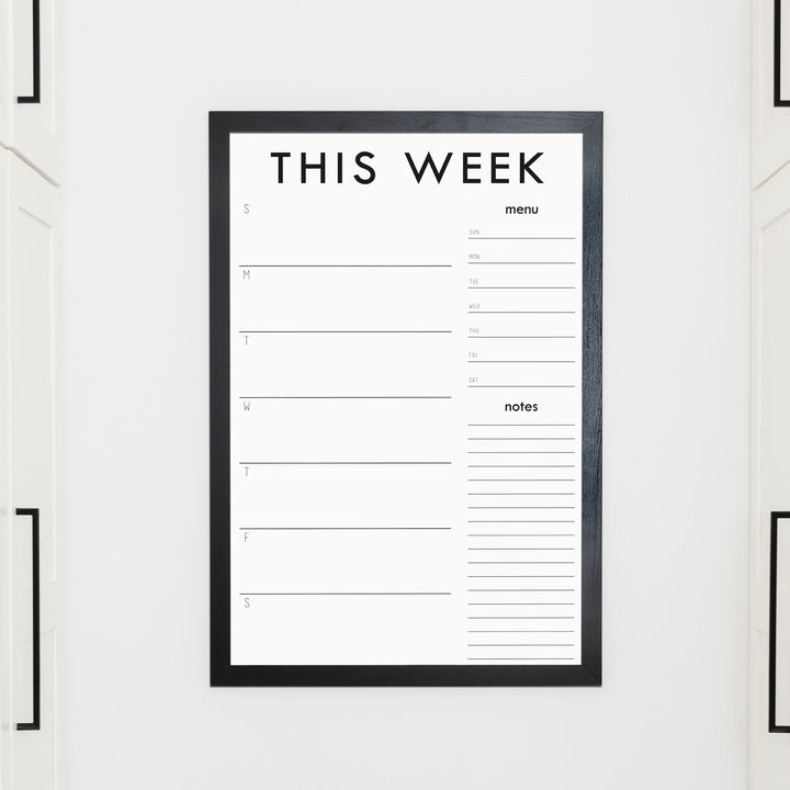 A framed whiteboard weekly calender hanging on the wall