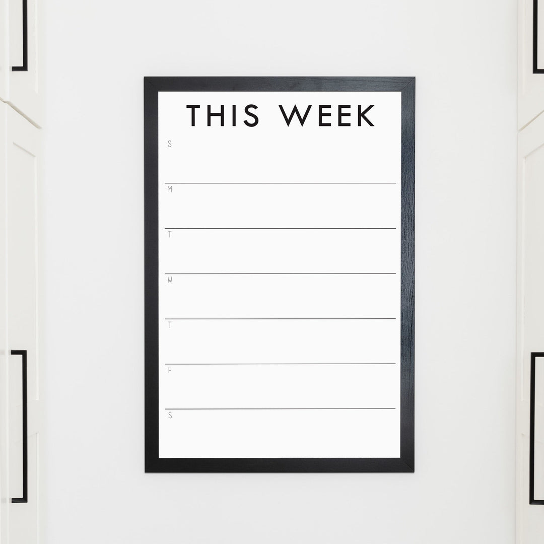 A framed whiteboard weekly calender hanging on the wall