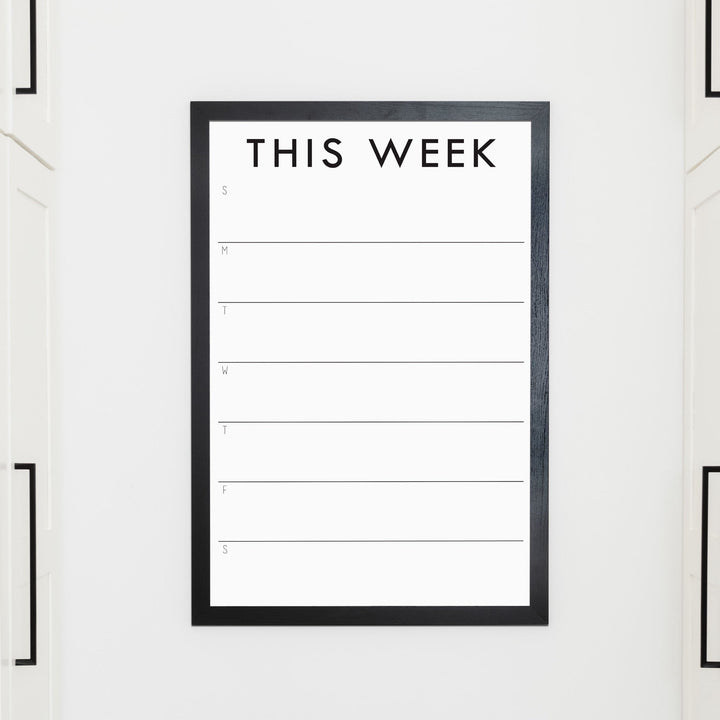 A framed whiteboard weekly calender hanging on the wall
