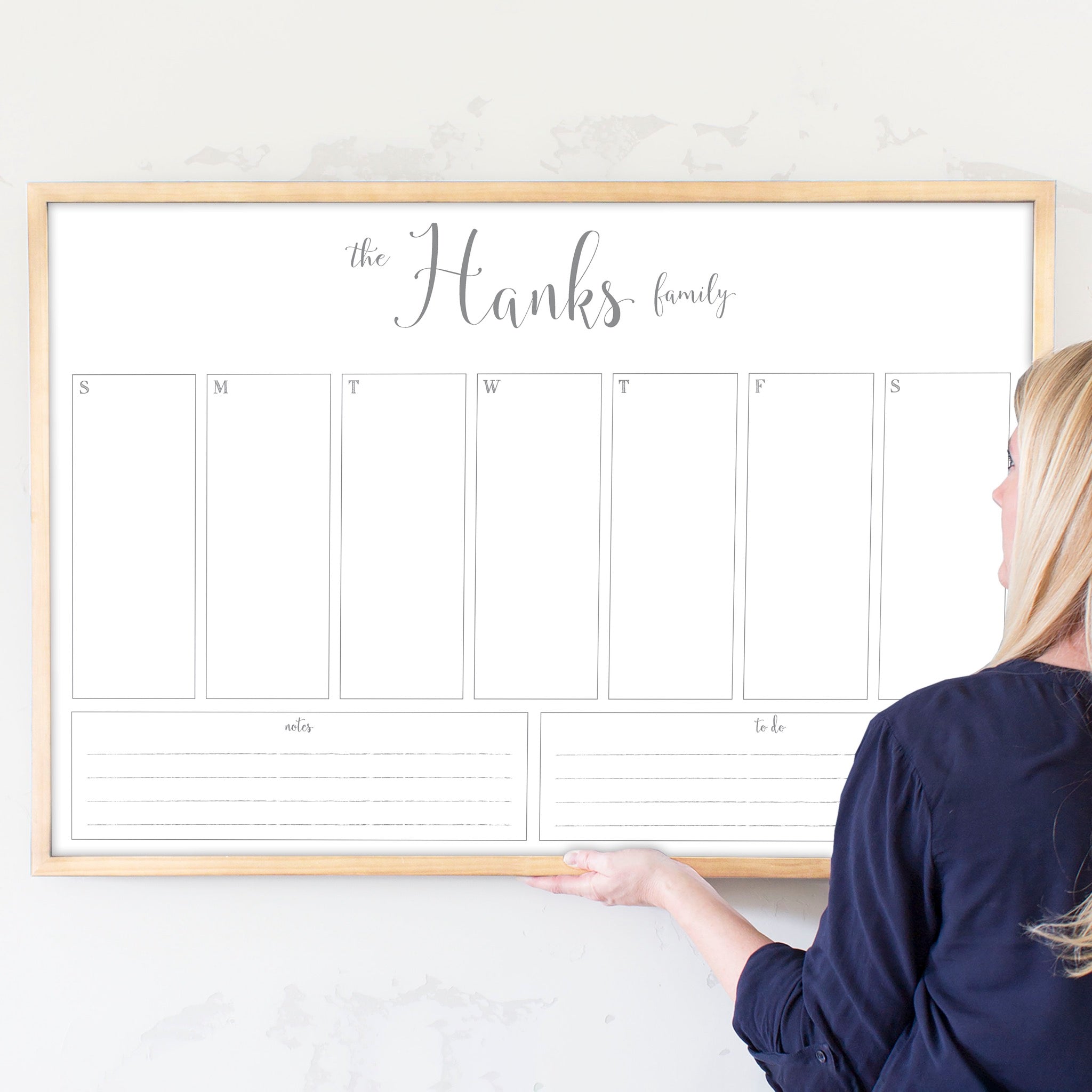 A framed whiteboard weekly calender hanging on the wall