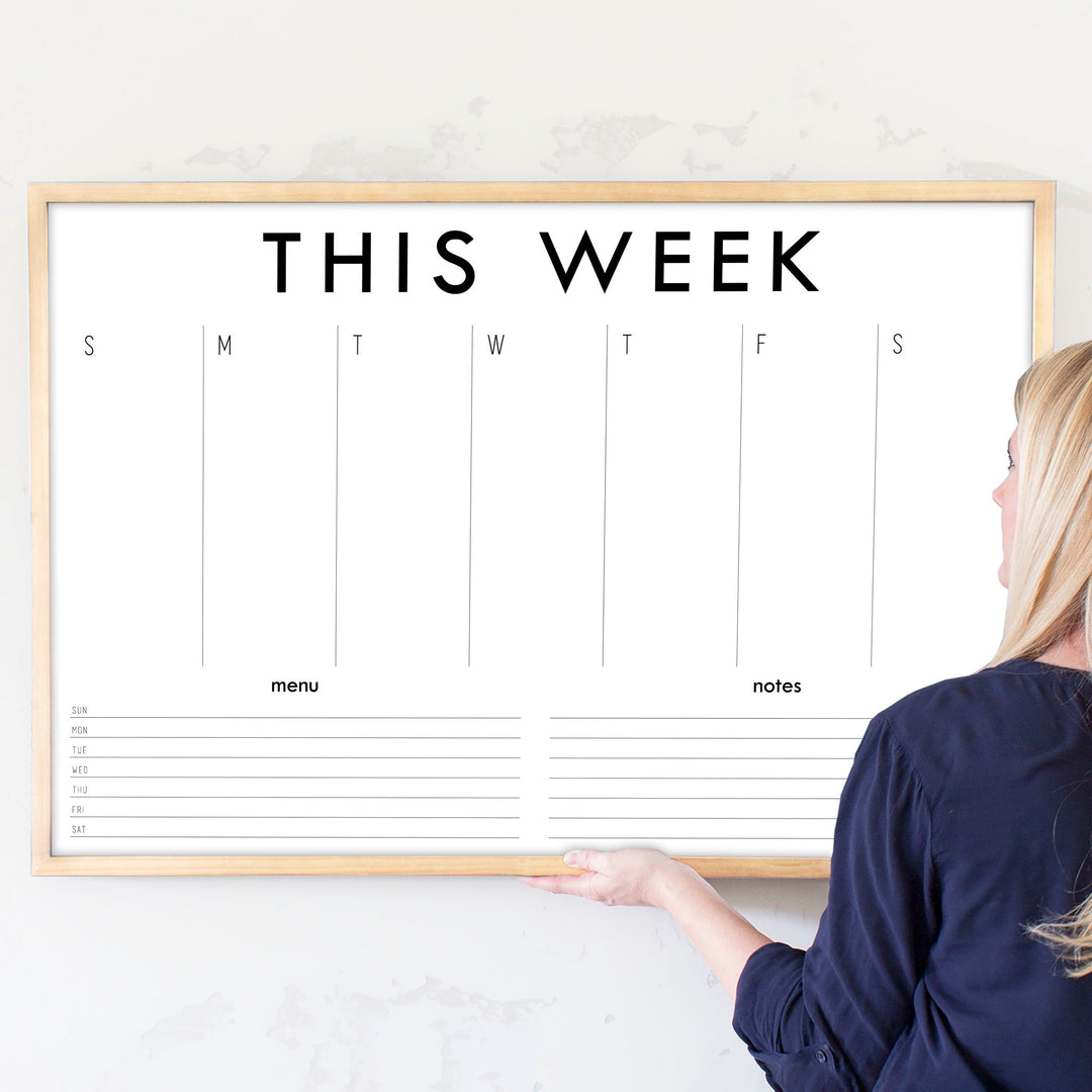 A framed whiteboard weekly calender hanging on the wall