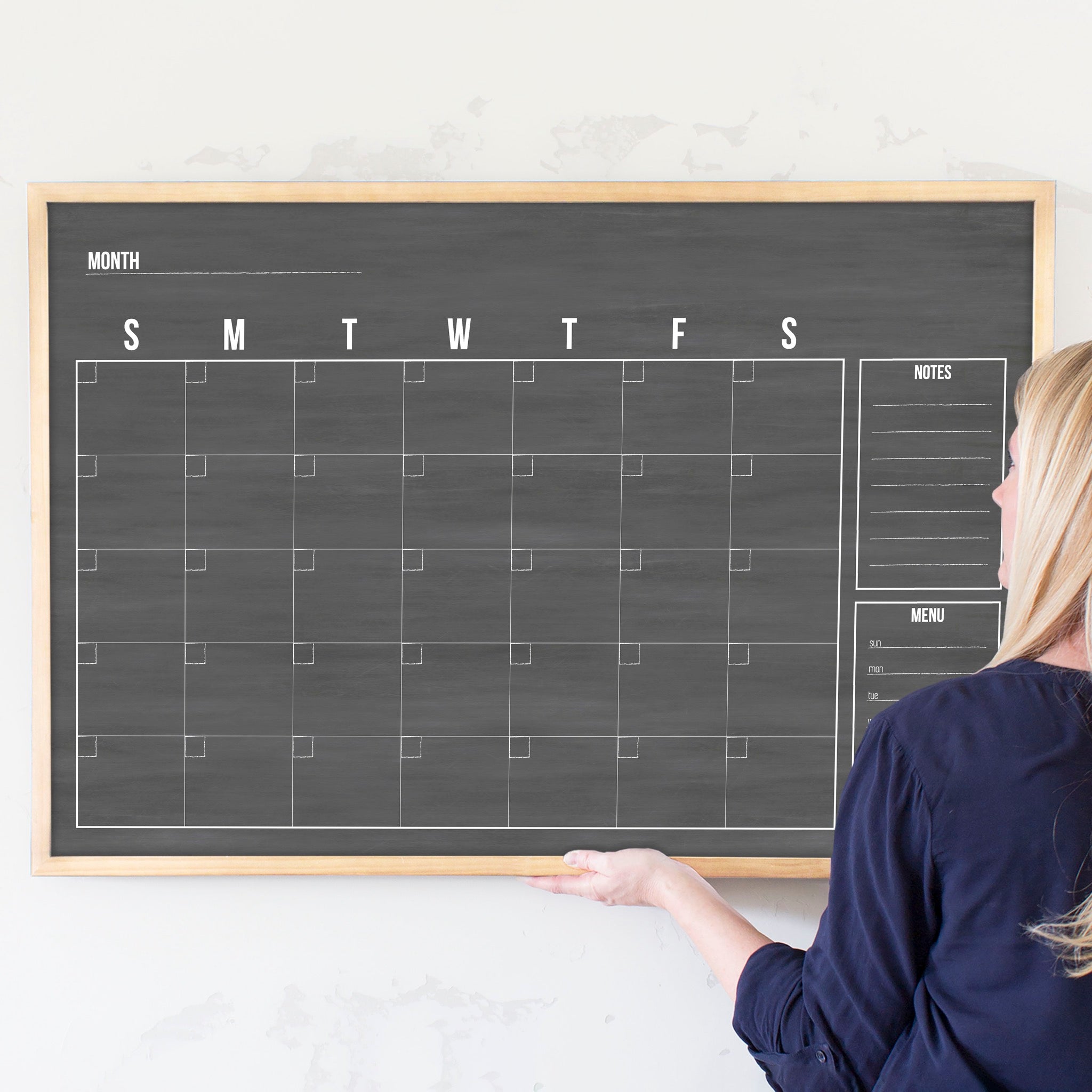 A framed dry-erase monthly calender with a chalkboard look hanging on the wall
