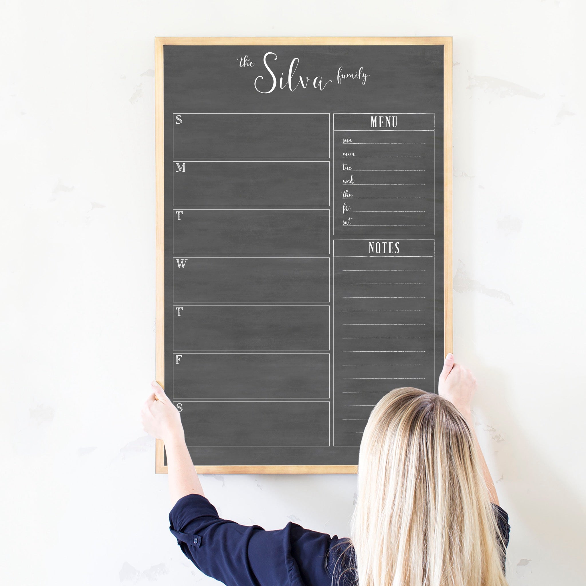 A framed dry-erase weekly calender with a chalkboard look hanging on the wall