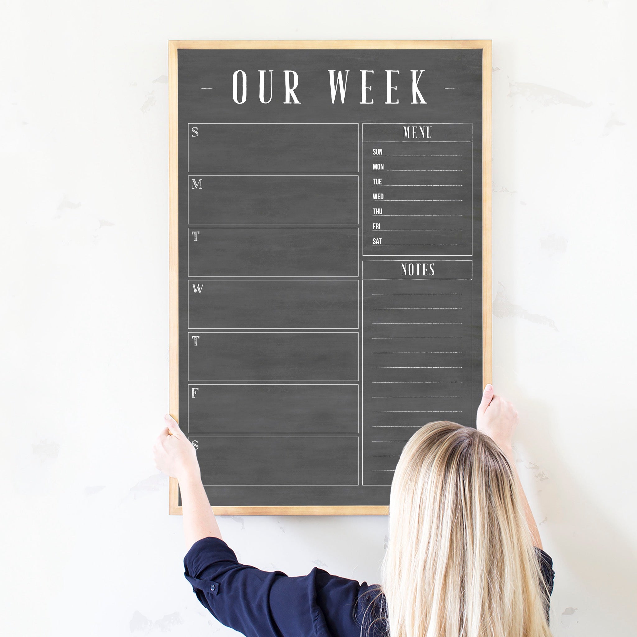 A framed dry-erase weekly calender with a chalkboard look hanging on the wall