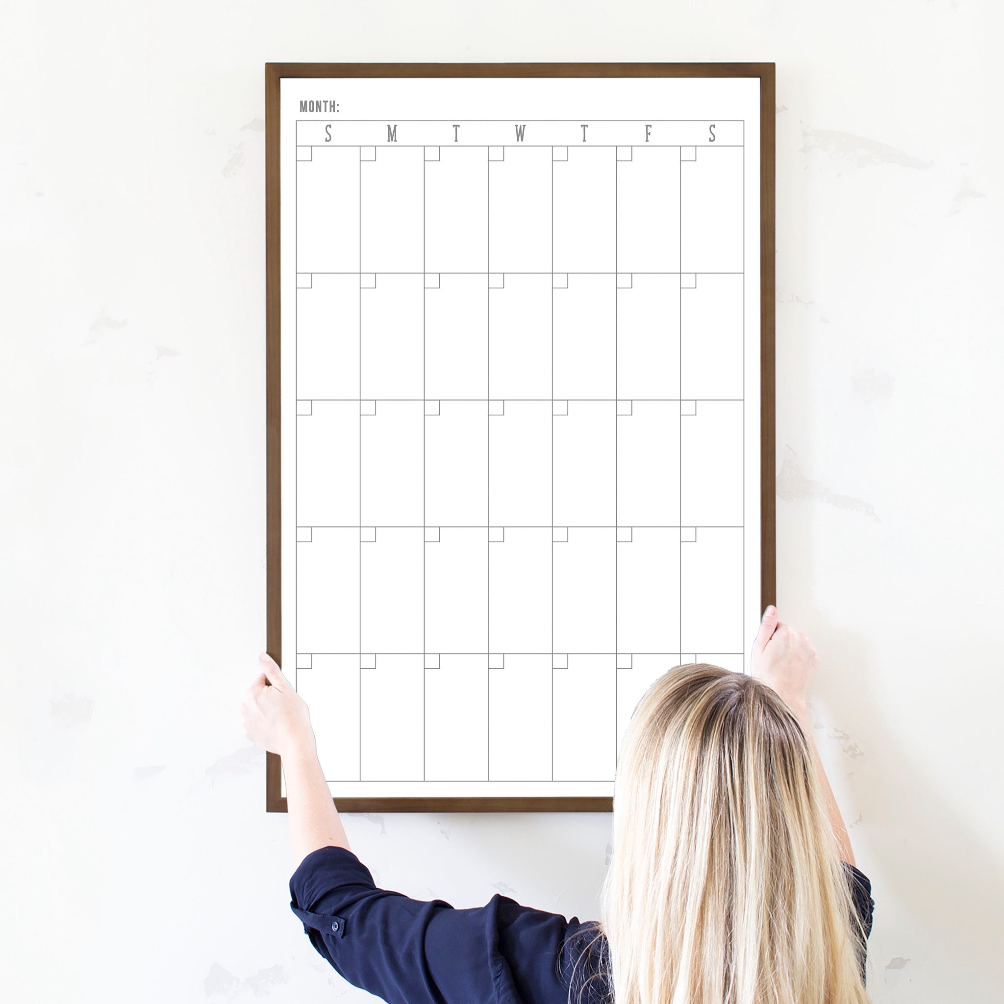 A framed dry-erase monthly calender with a chalkboard look hanging on the wall