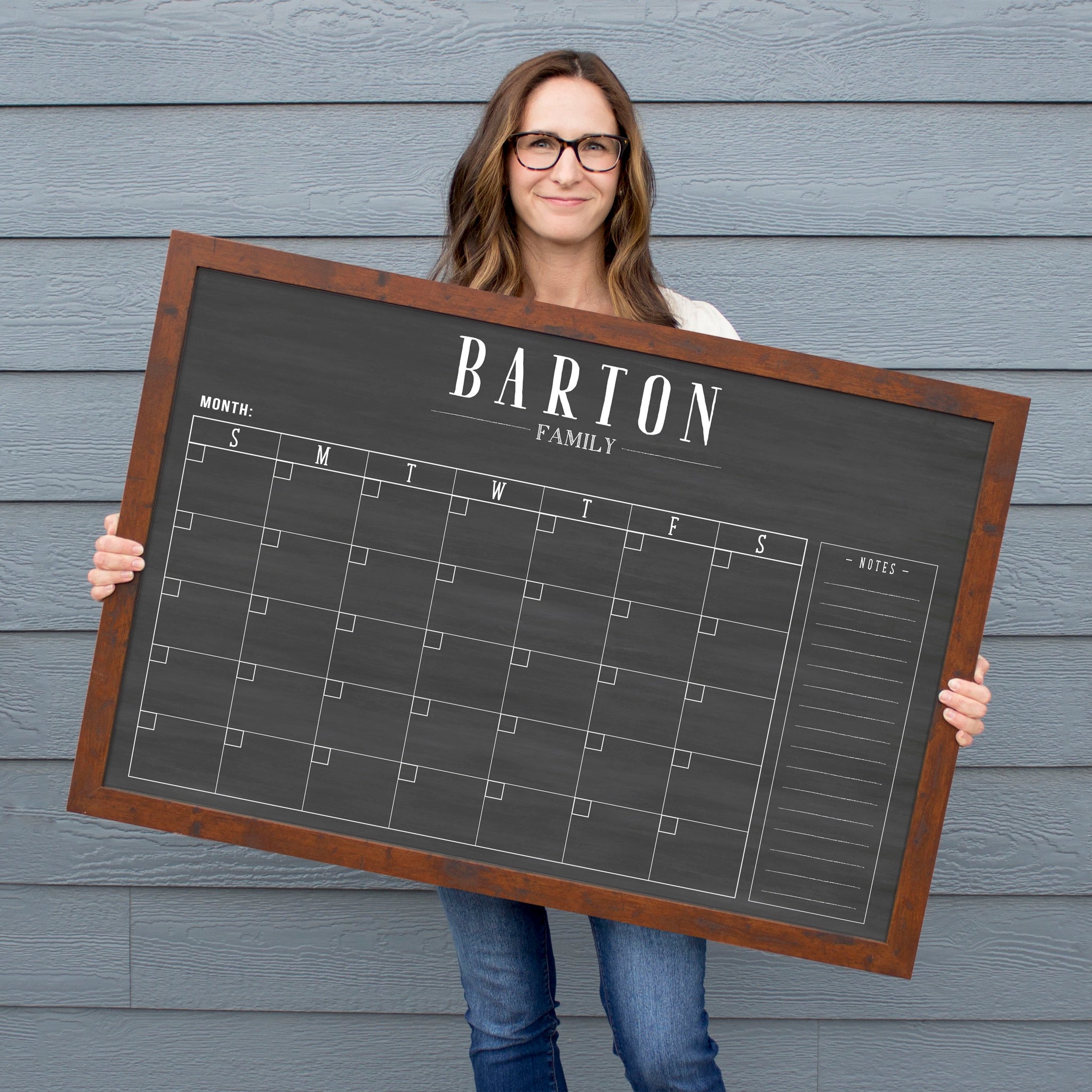 A framed dry-erase monthly calender with a chalkboard look hanging on the wall