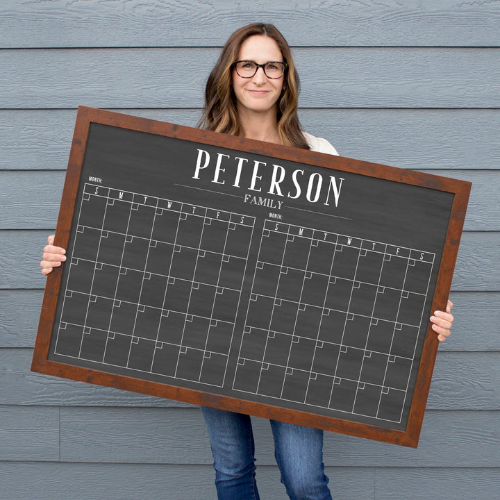 A framed chalkboard dry-erase calendar with a two month design format hanging on the wall
