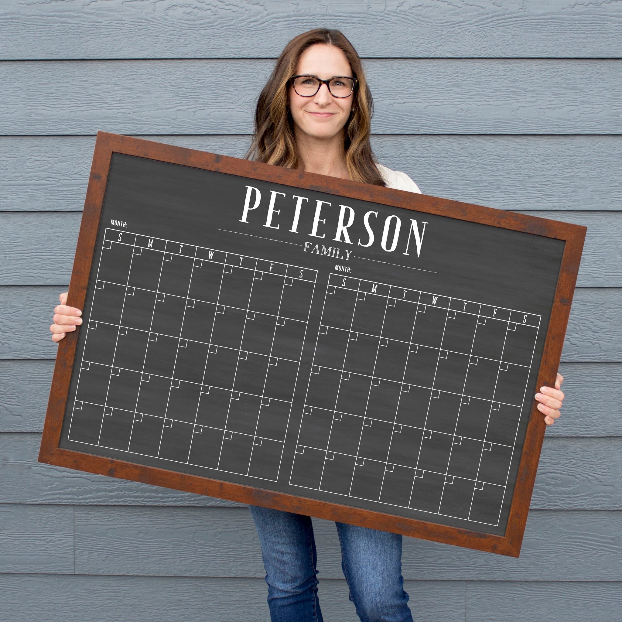 A framed chalkboard dry-erase calendar with a two month design format hanging on the wall