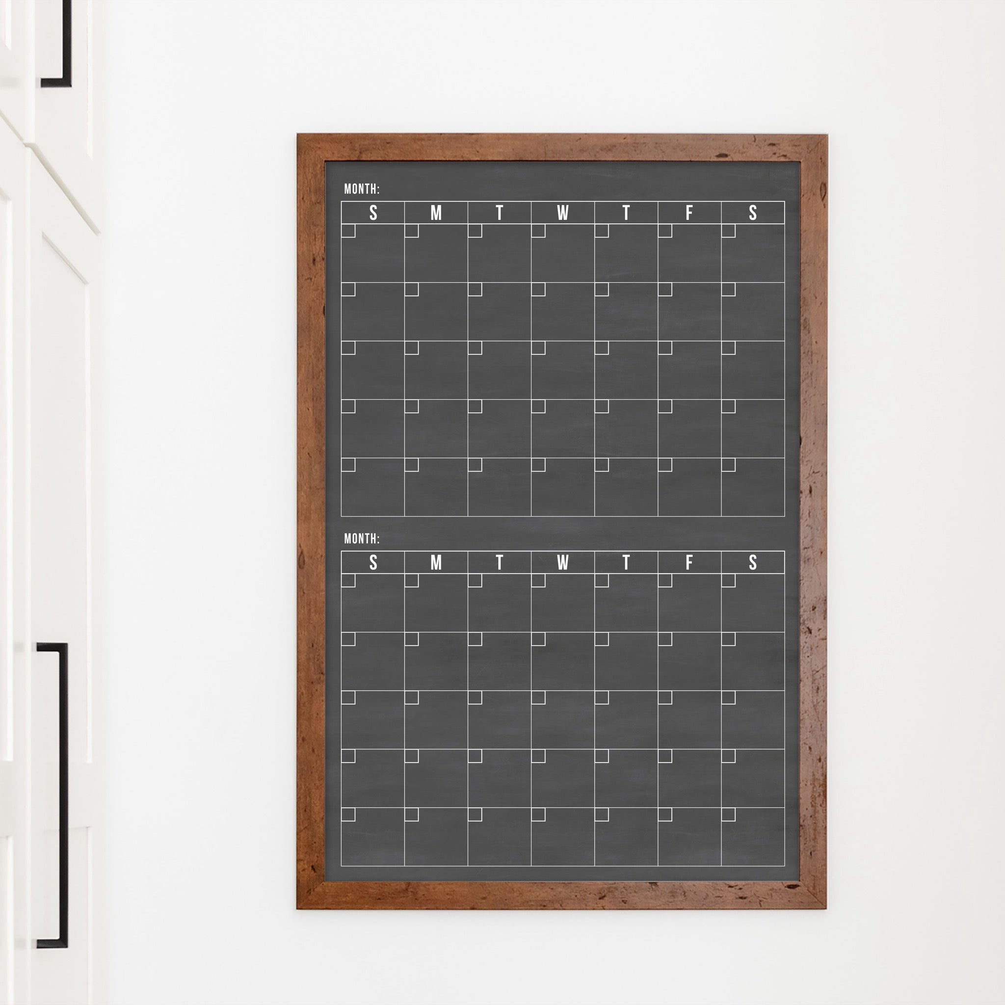 A framed chalkboard dry-erase calendar with a two month design format hanging on the wall