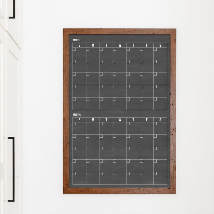 A framed chalkboard dry-erase calendar with a two month design format hanging on the wall