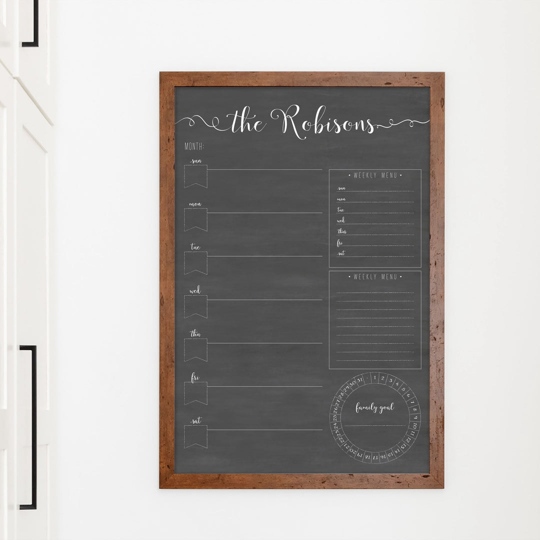 A framed dry-erase weekly calender with a chalkboard look hanging on the wall